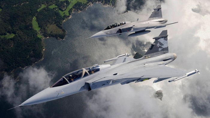 Two JAS 39 Gripen fighter jets flying over water and land