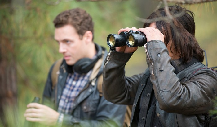 Two men in a forest, one using binoculars