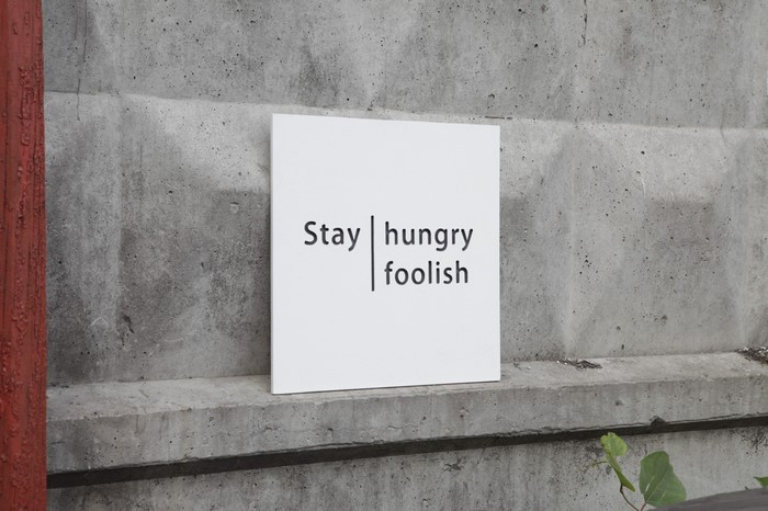 White sign with quote 'Stay hungry foolish' on concrete wall
