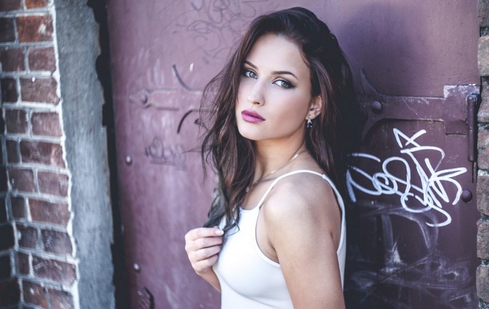 Woman with long brown hair leaning against a graffiti-covered door