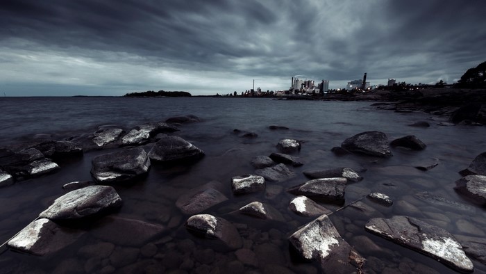 Rocky shore with industrial cityscape under stormy clouds