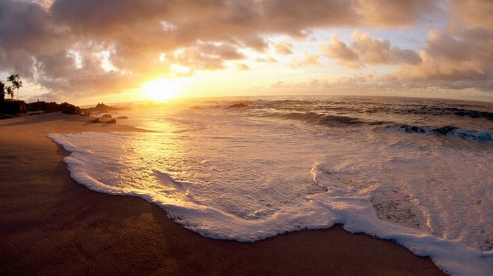 Sunset over a beach with waves and clouds
