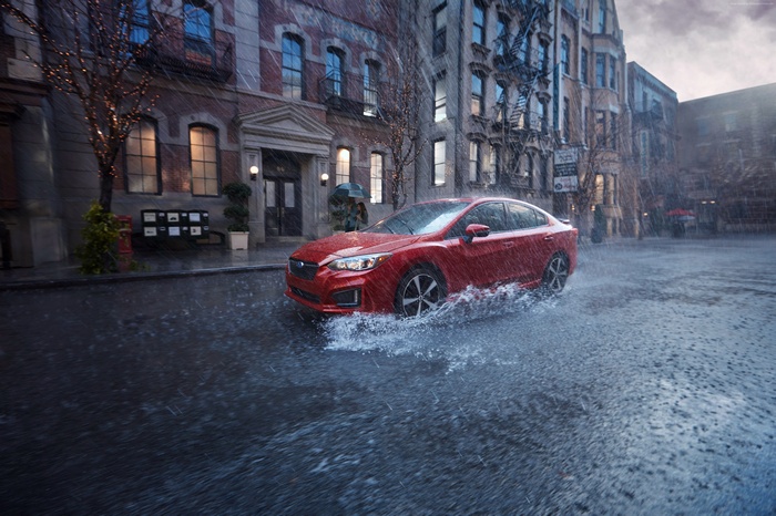 Red Subaru Impreza sedan driving through rain in city