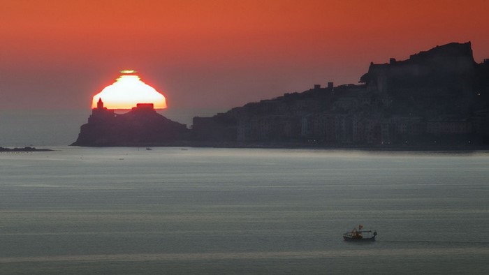 Sunset over a coastal town and sea with a boat