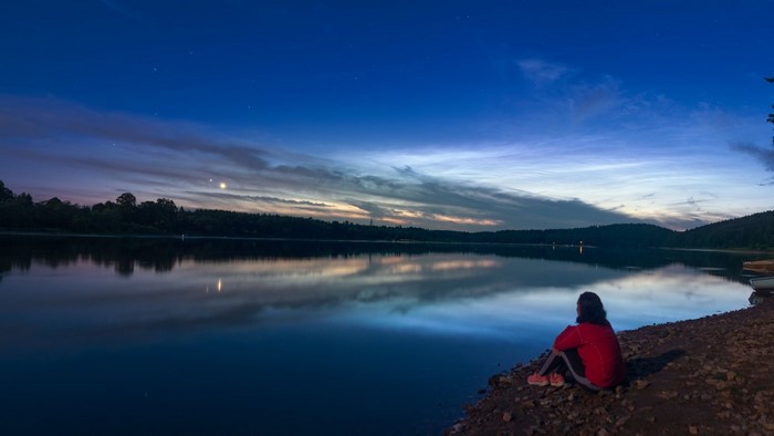 Person sitting by a lake at dusk with Jupiter and Venus