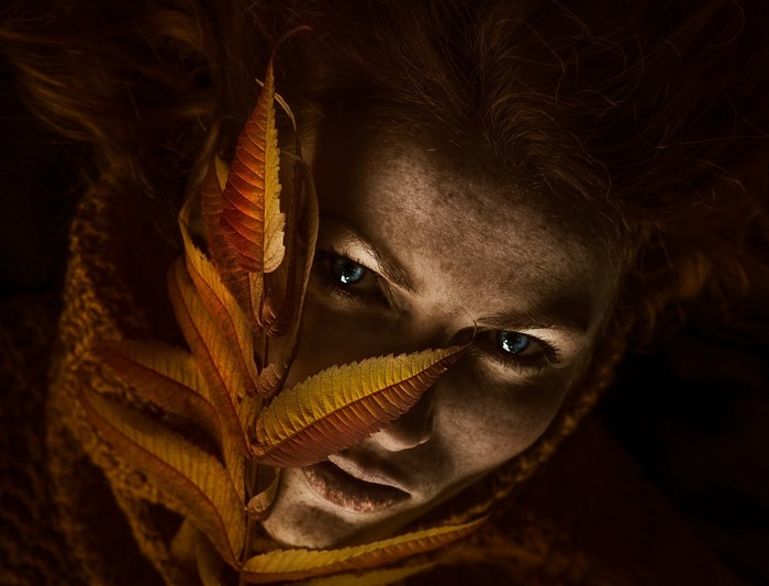 Woman with autumn leaves covering her face