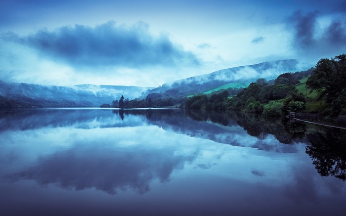 Misty mountains reflected in a calm lake at dawn