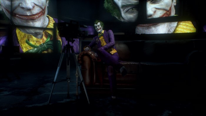 Joker from Batman sitting on a couch with screens behind him