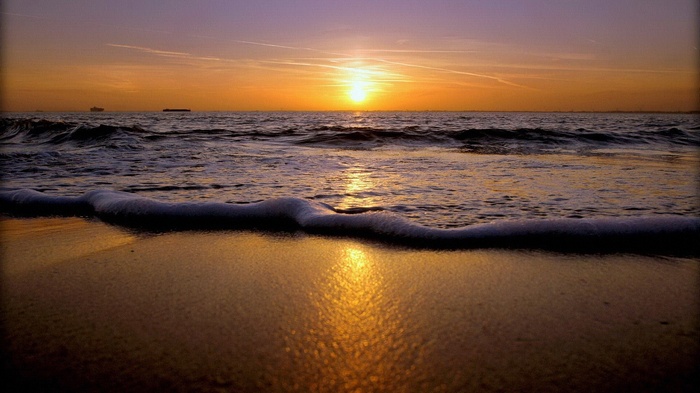 Sunset over the ocean with waves and ships