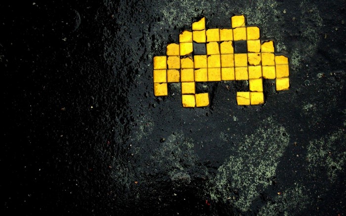 Yellow Space Invader pixel art on asphalt