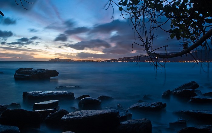 Rocks in the ocean at dusk with city lights on the horizon