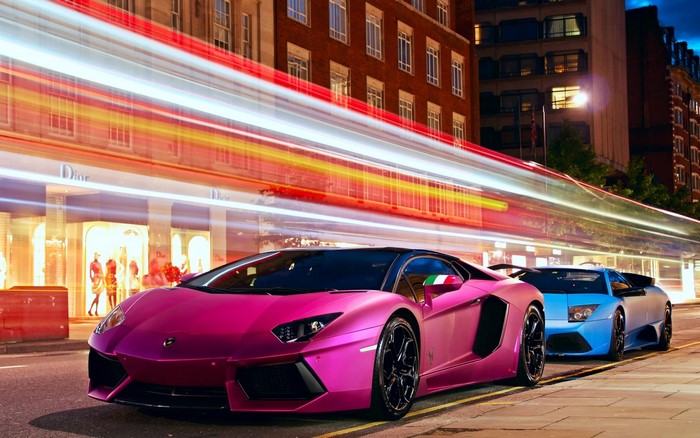 Pink and blue Lamborghinis parked on a city street at night