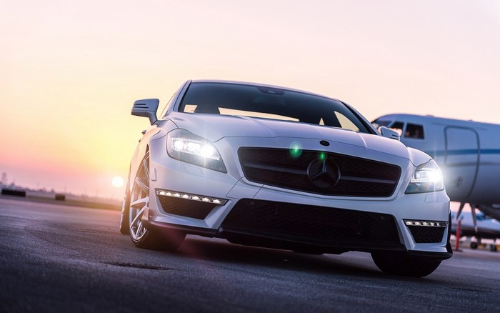 White Mercedes-Benz CLS parked near a private jet at sunset