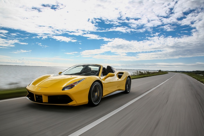 Yellow Ferrari 488 Spider driving on a road