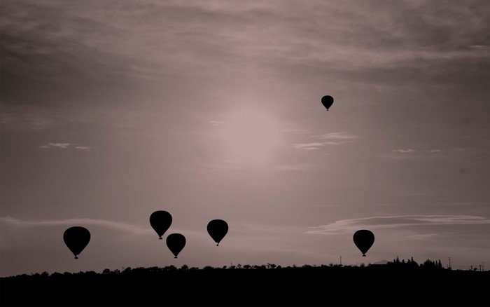 Hot air balloons flying over a silhouetted landscape at dawn