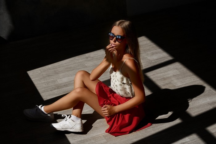 Young woman in sunglasses and red skirt sitting on wooden floor