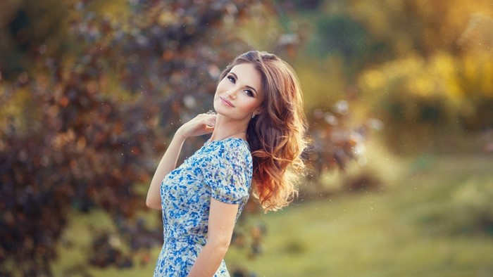 Woman in blue floral dress outdoors with bokeh background