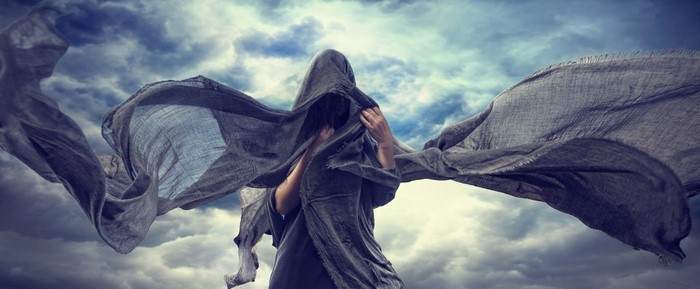 Person in dark robes with flowing fabric against cloudy sky