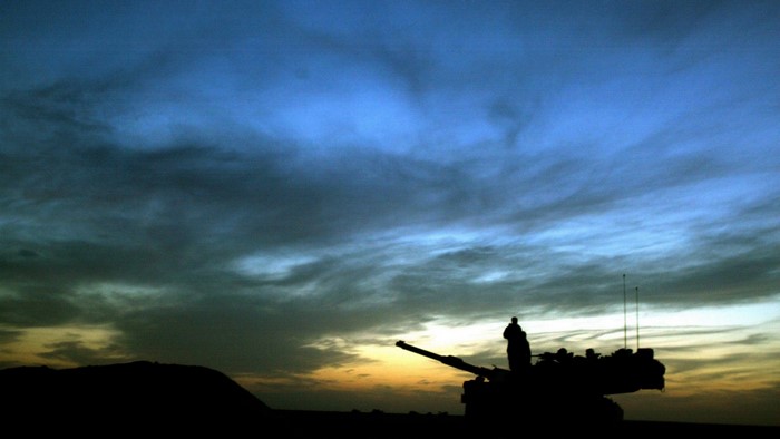 Silhouette of a tank and a person against a sunset sky