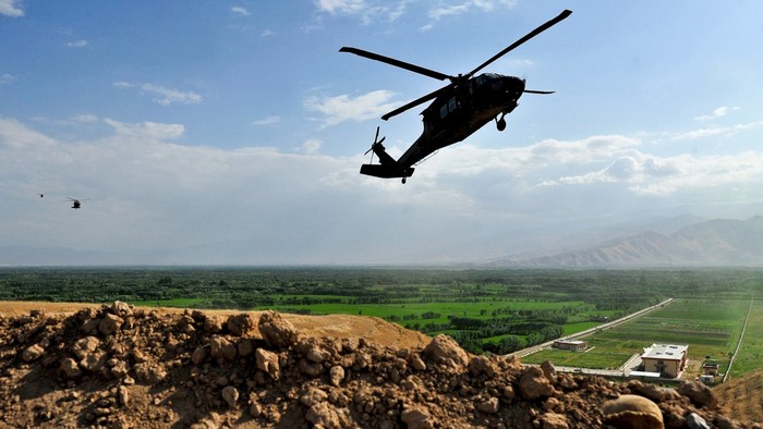 Two military helicopters flying over a landscape