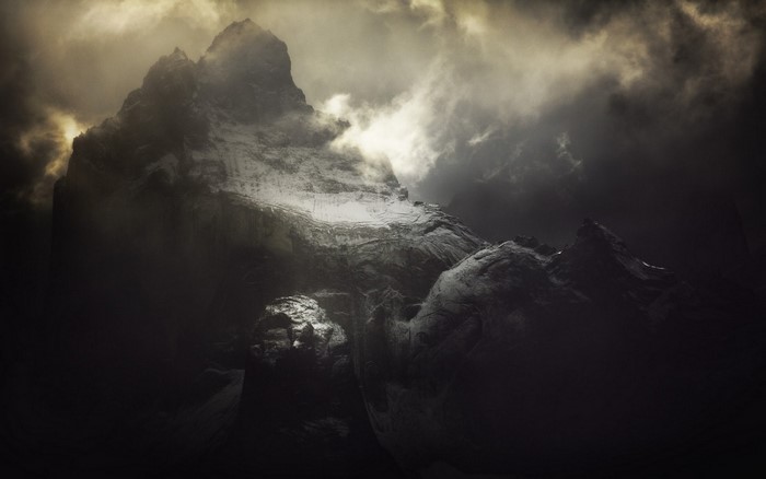 Dark, misty mountains with sunlight breaking through clouds