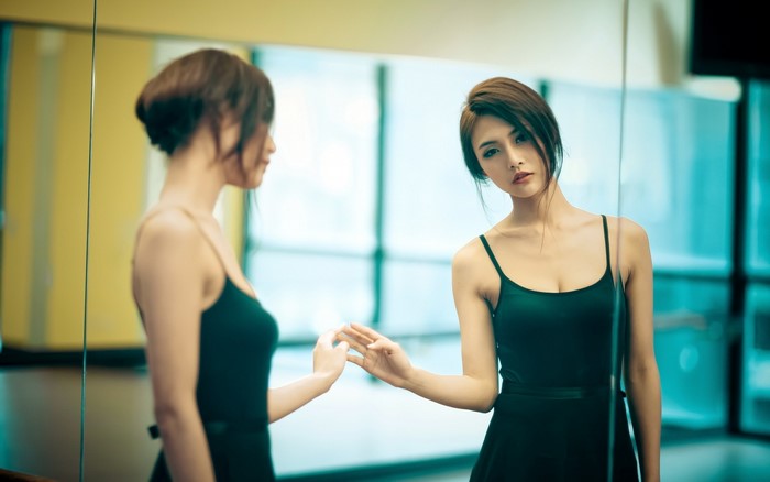 Asian woman in black dress looking at her reflection