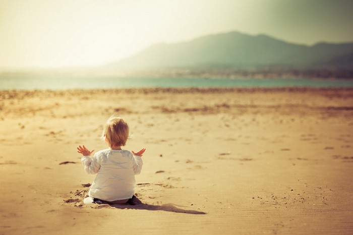 Baby sitting on a sandy beach looking at the ocean
