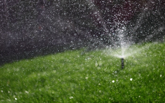Sprinkler watering a green lawn with water drops