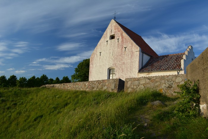White church with red roof on a grassy hill under a blue sky