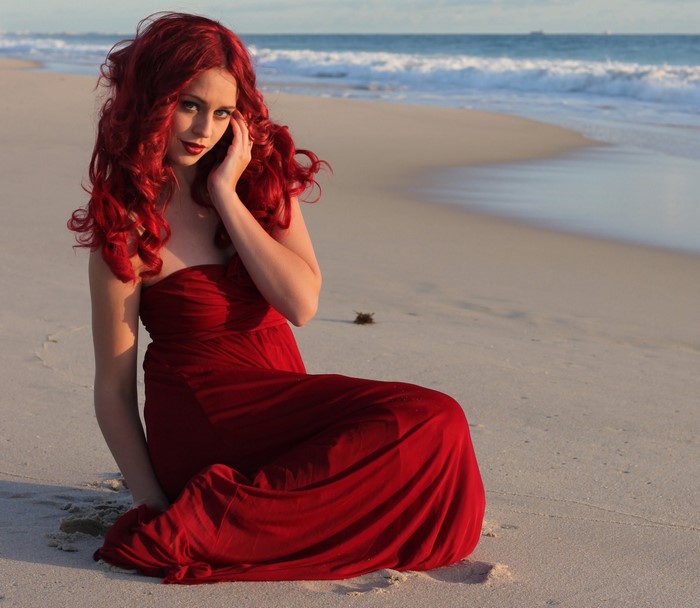 Redhead Woman in Elegant Red Dress Sitting on Beach