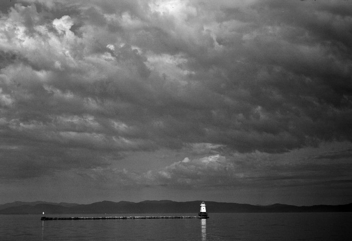 Monochrome landscape with lighthouse on a pier under cloudy sky