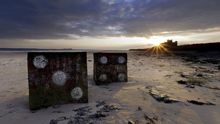 Dice on a beach at sunset with castle in background
