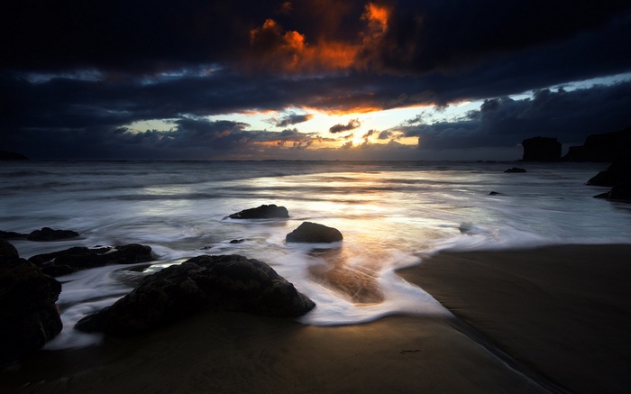 Dark beach with waves and rocks at sunset