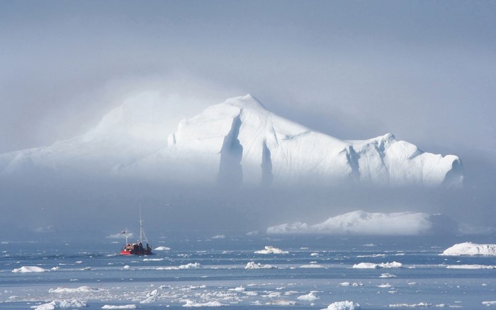 Red boat navigates through icebergs in foggy Arctic waters