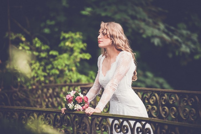 Bride in a white lace dress holding a bouquet on a bridge