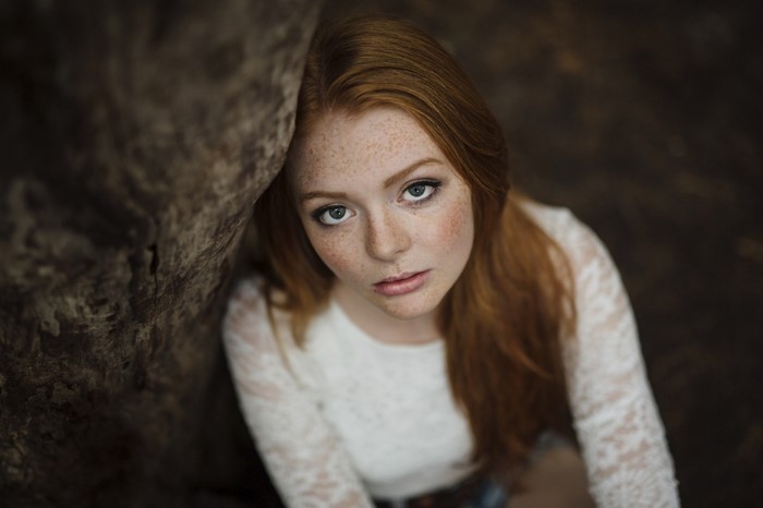 Redhead woman with freckles leaning on a tree