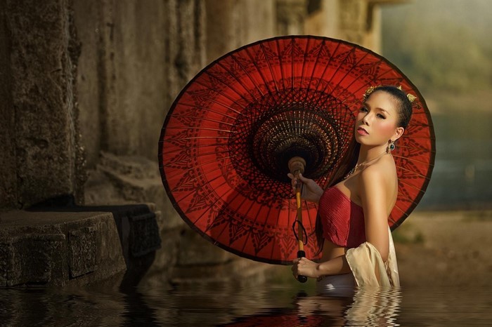 Woman in red top holding a red parasol in water