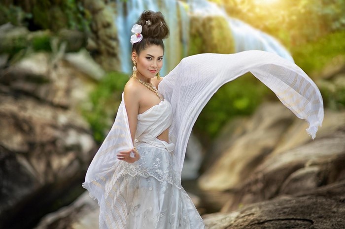 Woman in traditional white dress with flowing fabric near waterfall