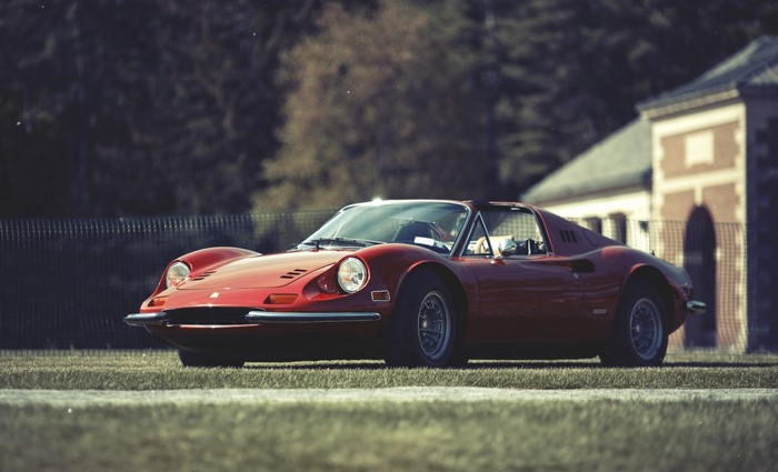Red Ferrari Dino parked on grass near a building