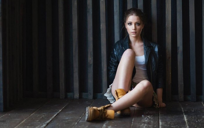Woman in leather jacket and white top sitting on floor