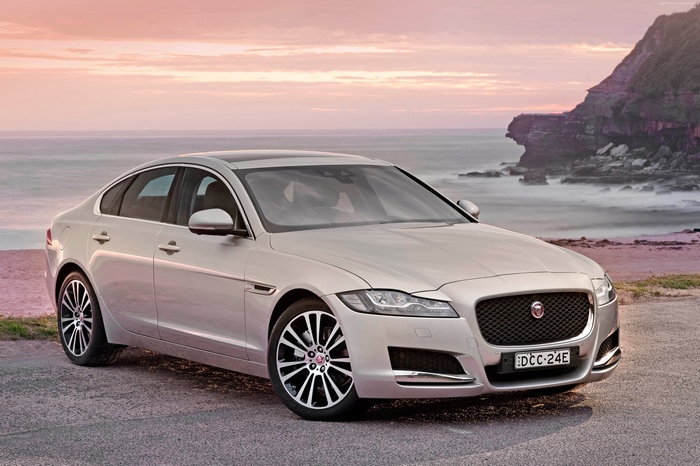 Silver Jaguar XF Portfolio sedan on a beach at sunset