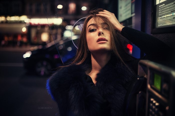 Woman in fur coat by payphone at night