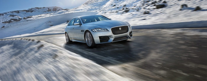 Silver Jaguar XF R-Sport driving on a snowy mountain road