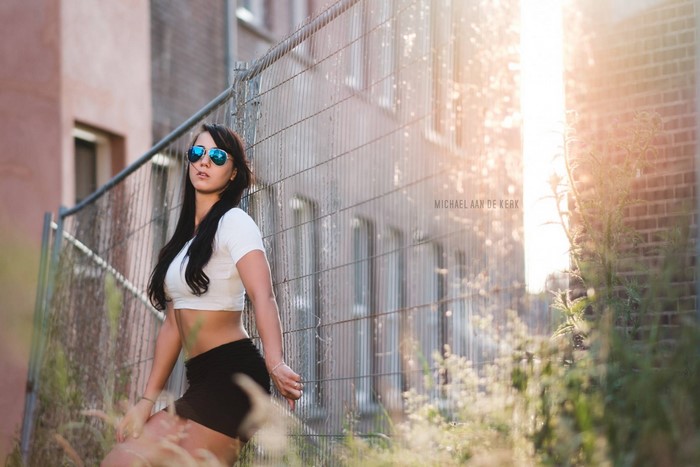 Woman in crop top and shorts posing by fence