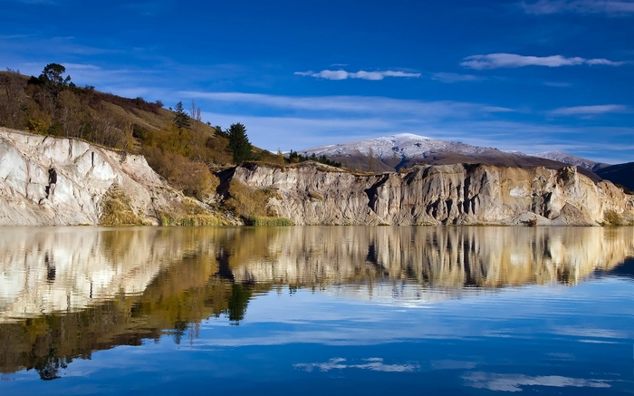 Lake reflecting cliffs and snow-capped mountains under blue sky