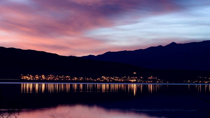 City lights reflected on a lake at sunset with mountains