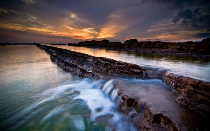 Rocky coastline with water flowing at sunset