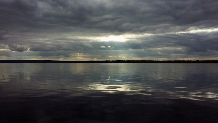 Dark clouds over a calm lake with distant shore