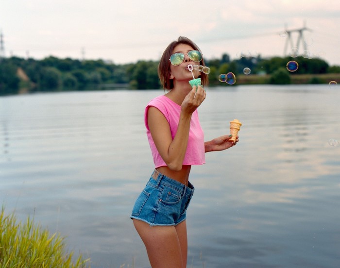 Woman blowing bubbles and holding ice cream cone by lake