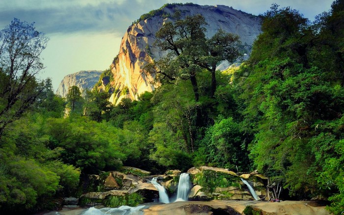 Waterfall flowing through a forest with a mountain backdrop